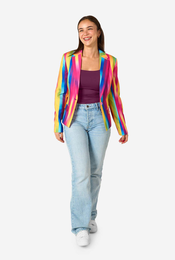 Woman wearing a colorful rainbow striped blazer and light blue jeans against a white background. Full body image.