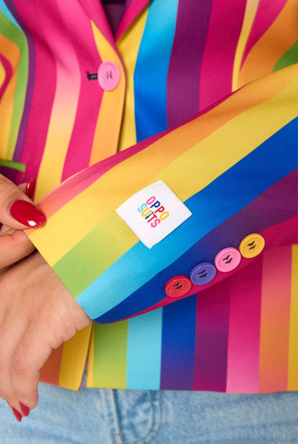Woman wearing a colorful rainbow striped blazer and light blue jeans against a white background.  Sleeve close up.