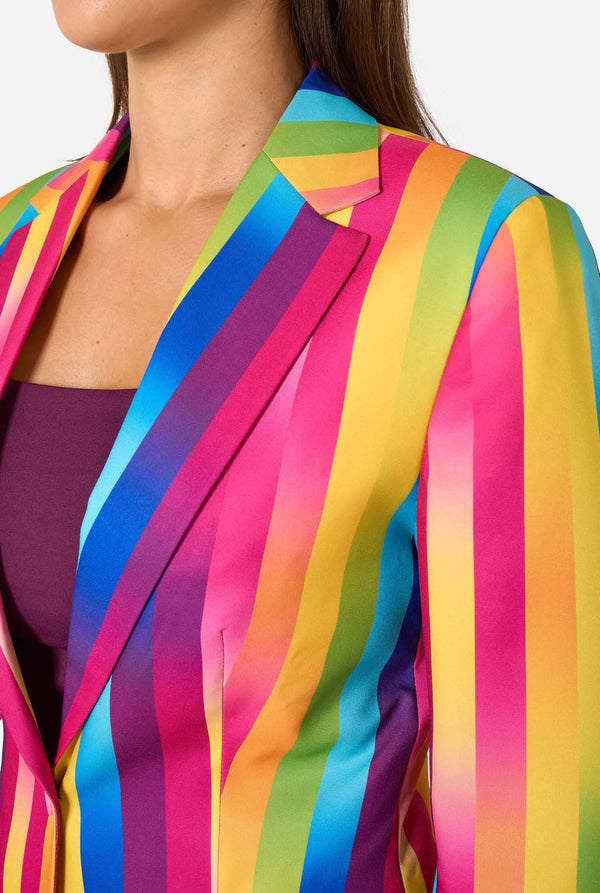 Woman wearing a colorful rainbow striped blazer and light blue jeans against a white background. Chest close up.