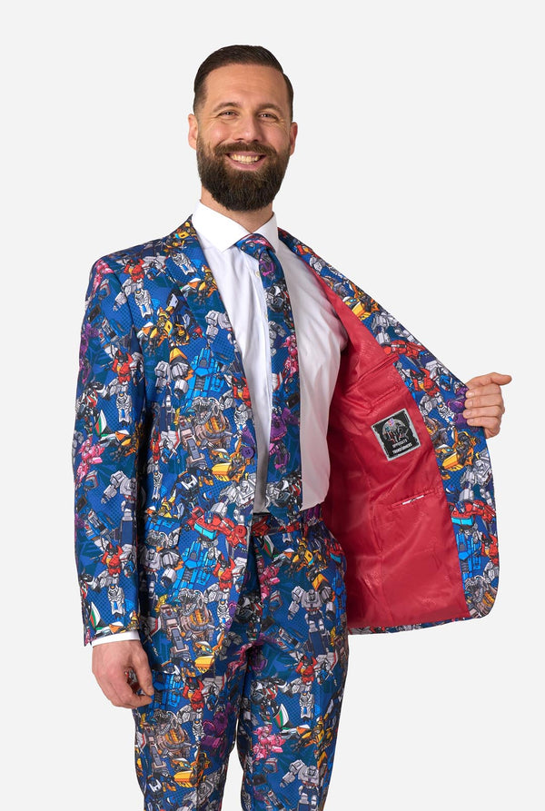 Man wearing a colorful suit with Transformer pattern on a light background. Holding one side of the jacket open.