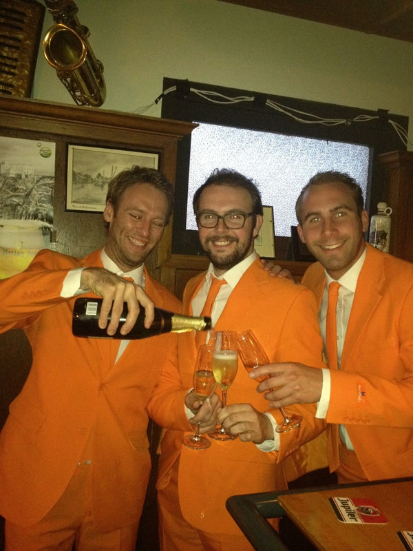 Image of the 3 founders of Opposuits in Orange suits drinking champagne.