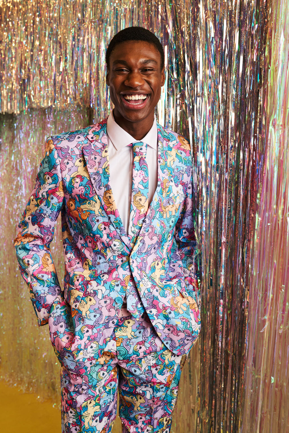 Man wearing a colorful My Little Pony suit with a patterned tie against a glittery gold background