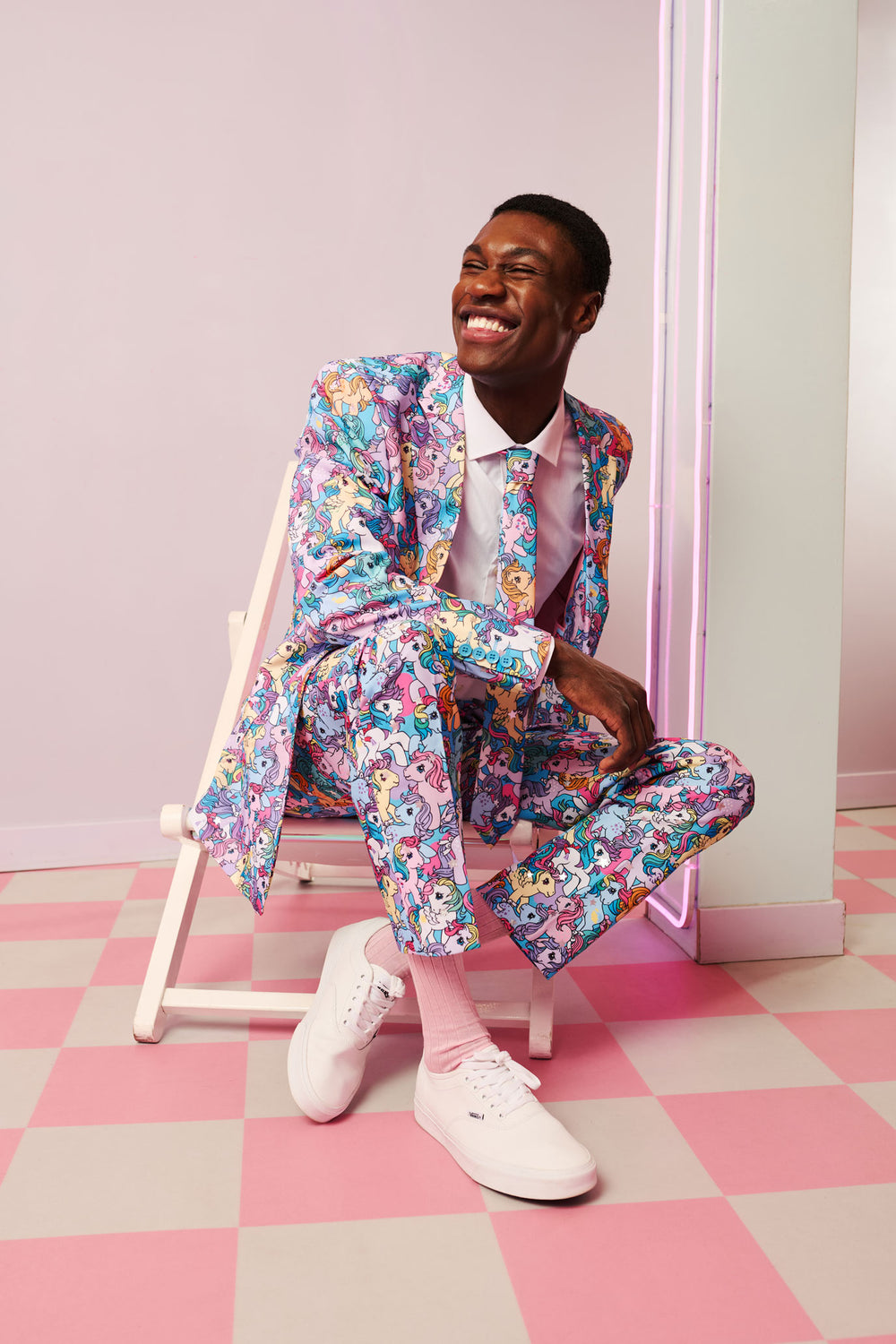 Man in a colorful My Little Pony pink suit sitting on a chair with a pink and white checkered floor.