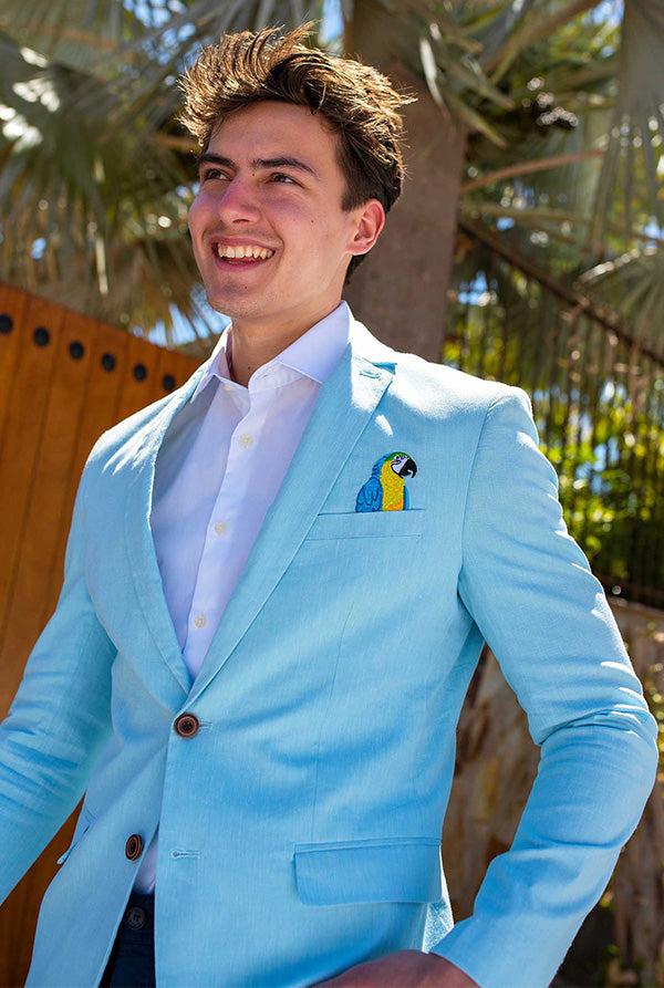 Man wearing a light blue suit with a parrot pocket square, standing outdoors.