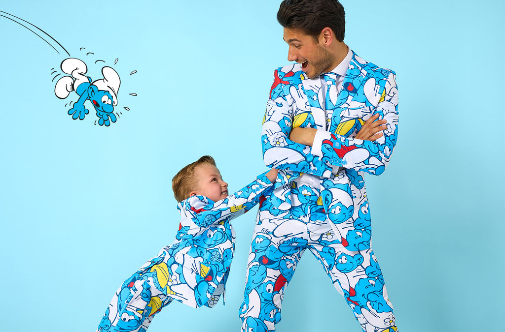 This is an image with a light blue background, a Smurf falling in the image on the left side, and a man and kid wearing a suit with an all-over Smurf suit. The kid is pushing the man.
