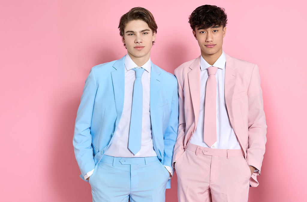 Image with pink background and two men wearing solid colored suit. The left wearing a light blue suit and the right wearing a pink suit.