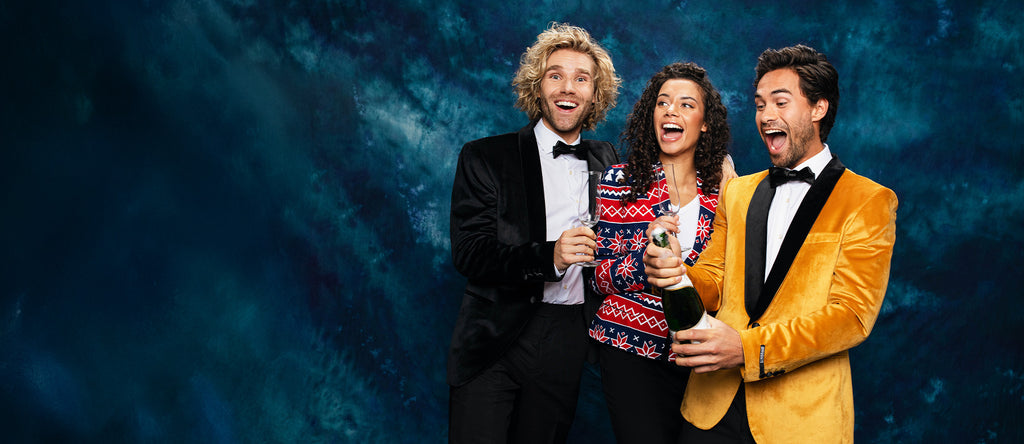 Image with blue background and 3 people wearing Christmas outfits. 1 man wearing black blazer, woman wearing Red and blue blazer and a man wearing a golden blazer.