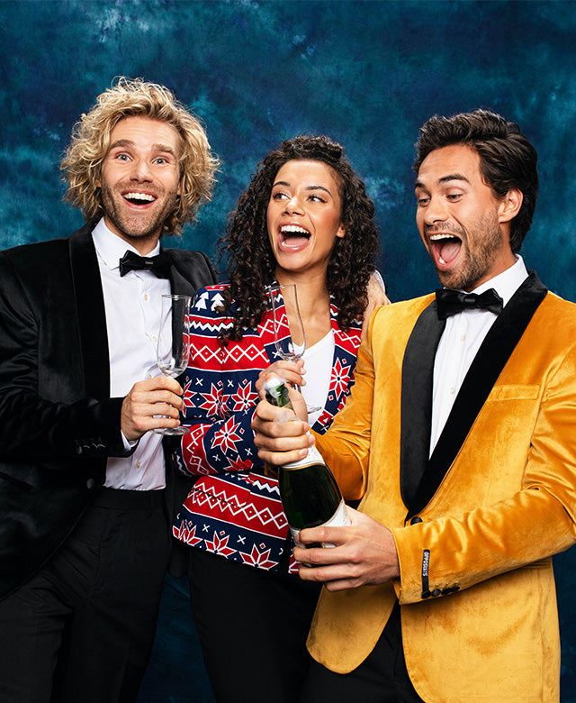 Image with blue background and 3 people wearing Christmas outfits. 1 man wearing black blazer, woman wearing Red and blue blazer and a man wearing a golden blazer.