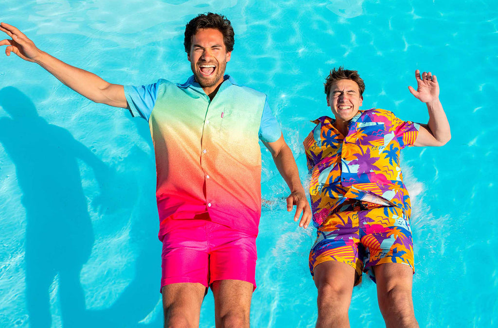 Image of two men falling in a swimming pool. Both of them are wearing colourful summer sets.