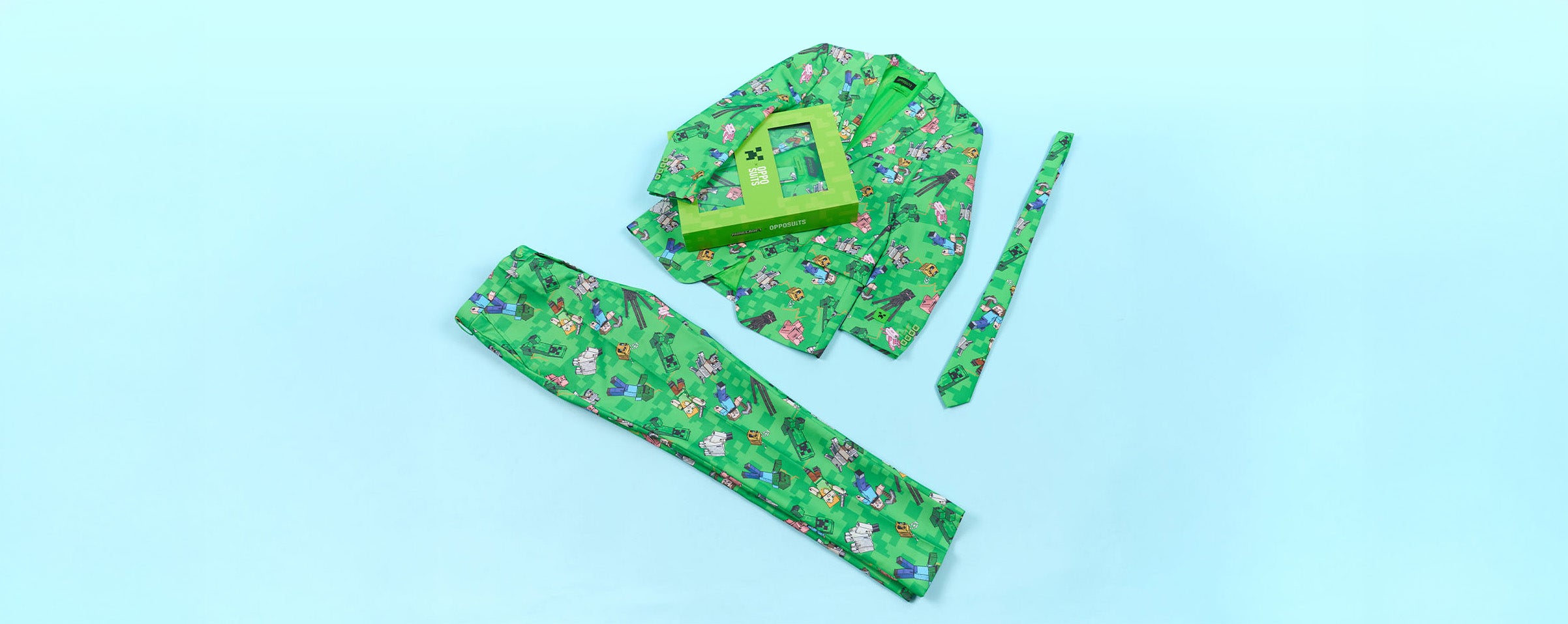 A green patterned, Minecraft themed fabric clothing set laid flat on a light blue background, including a long rectangular piece, a smaller matching strip, and a folded top with a green rectangular accessory placed on top.