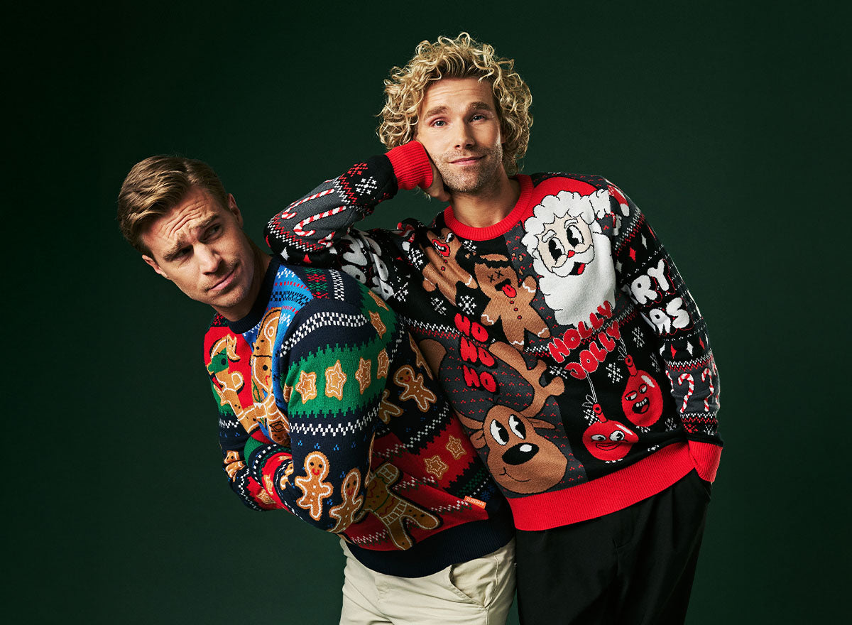 Image with dark green background and two men leaning against each other, wearing colorful Christmas sweaters.