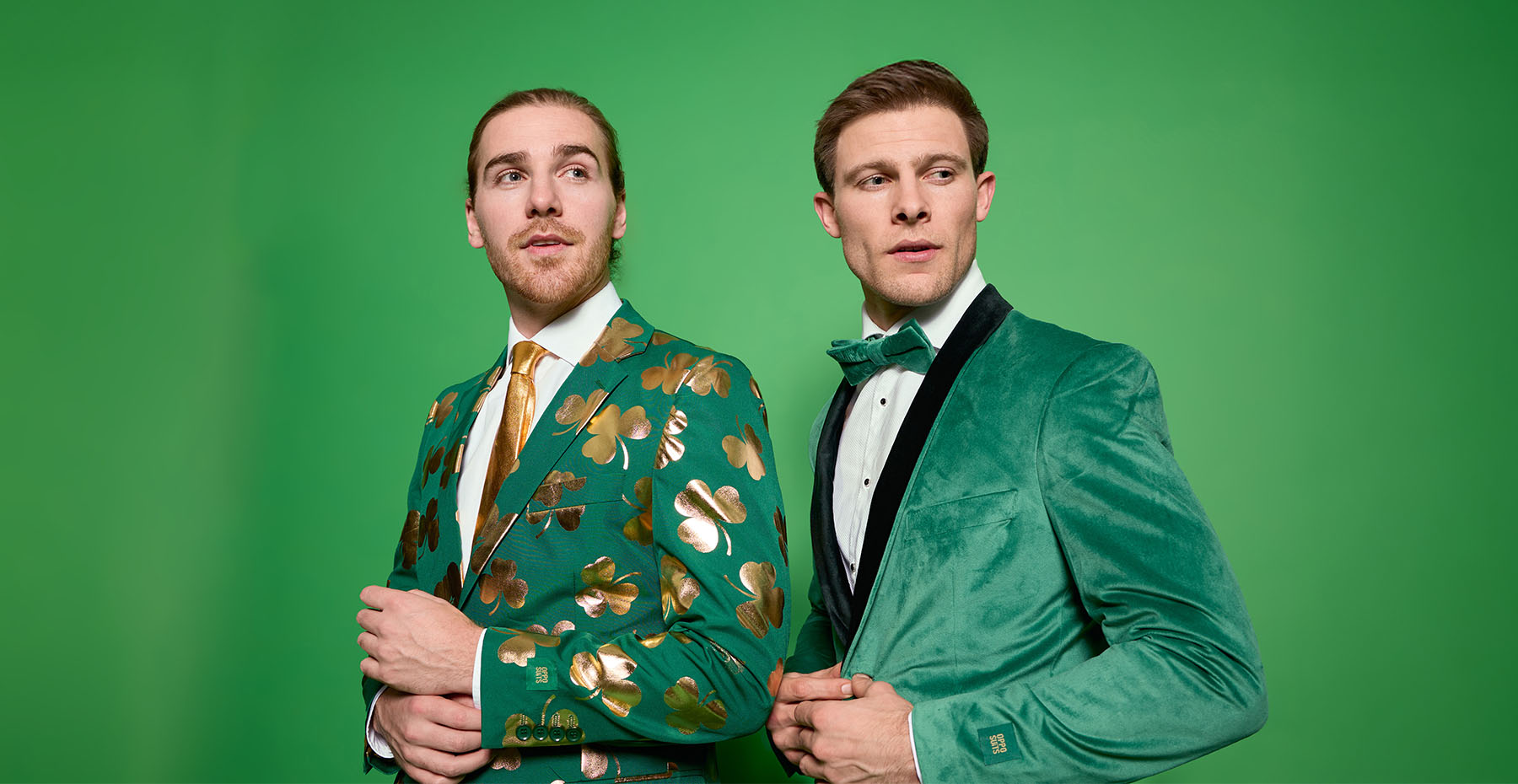 Image with green background and on the left a man wearing a green suit with golden clovers and on the right a man wearing a velvet green tuxedo.