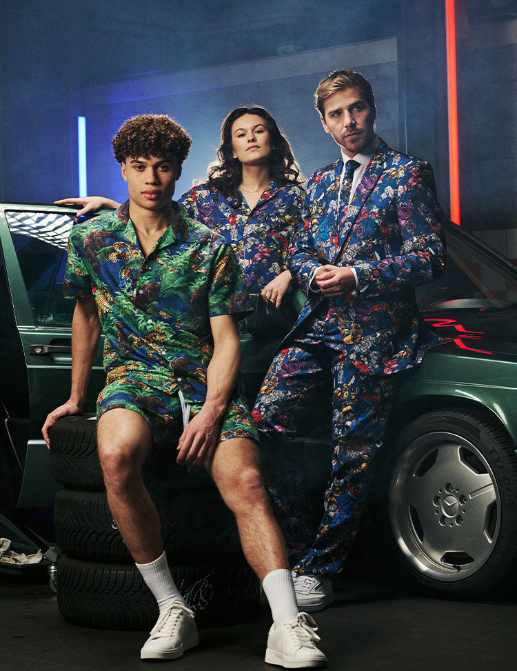 Image of garage with a car and a man wearing the OppoSuits Transformers suit, a man wearing a Transformers summer set and a woman wearing a Transformers Hawaiian.