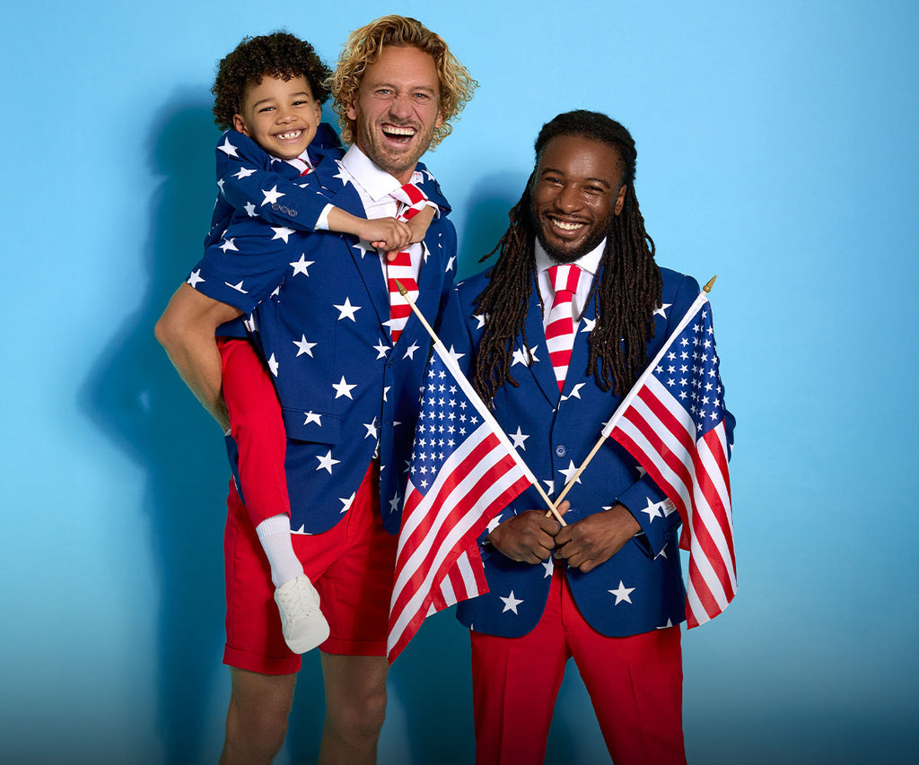 Image with light blue background and 2 men wearing a USA themed blue, red and white suit. One man carrying a kid on his back, the kid also wearing a USA themed suit