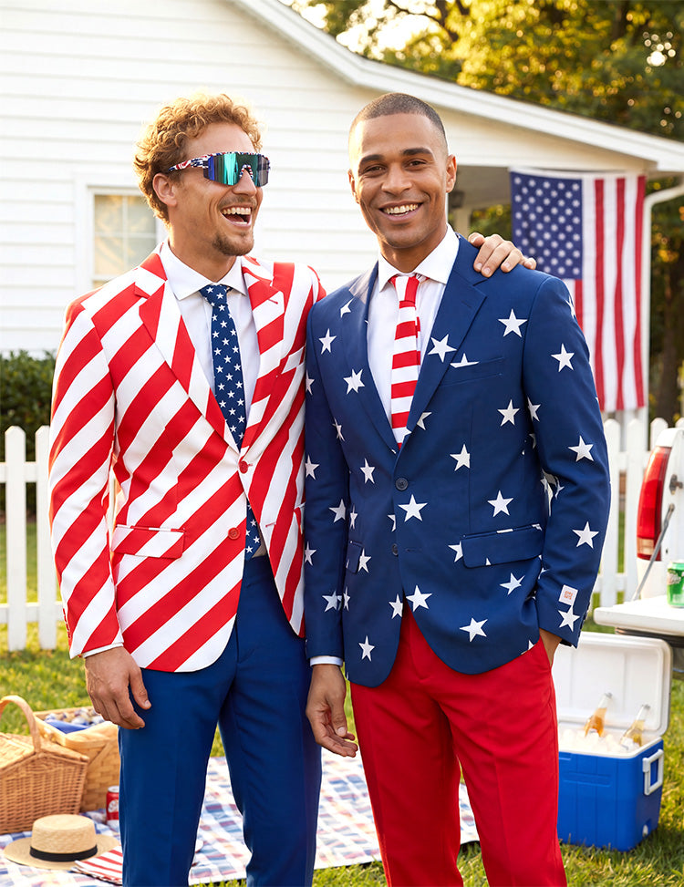 image of two men standing in front of a house in a garden wearing suits resembling the USA flag. Picknick set on the grass and american flag on the house.