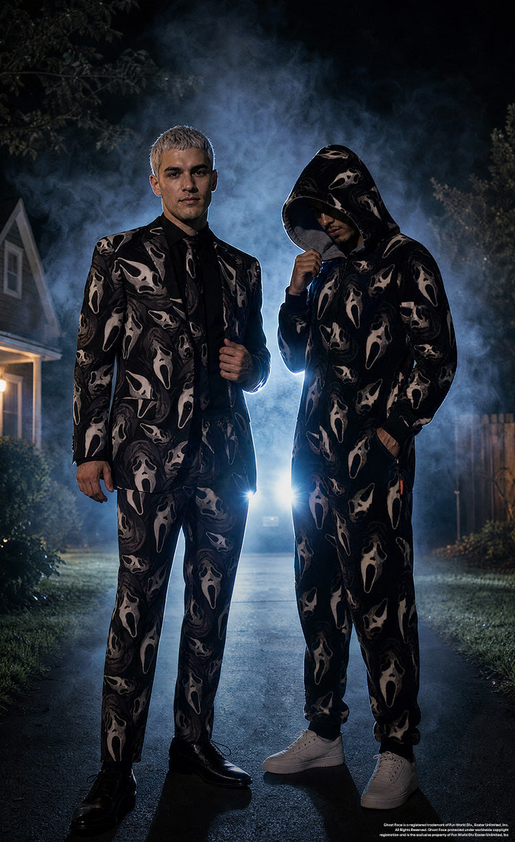 Two men wearing matching black-and-beige Ghostface-patterned outfits stand outside a house at night, surrounded by mist, trees, and dramatic blue backlighting.
