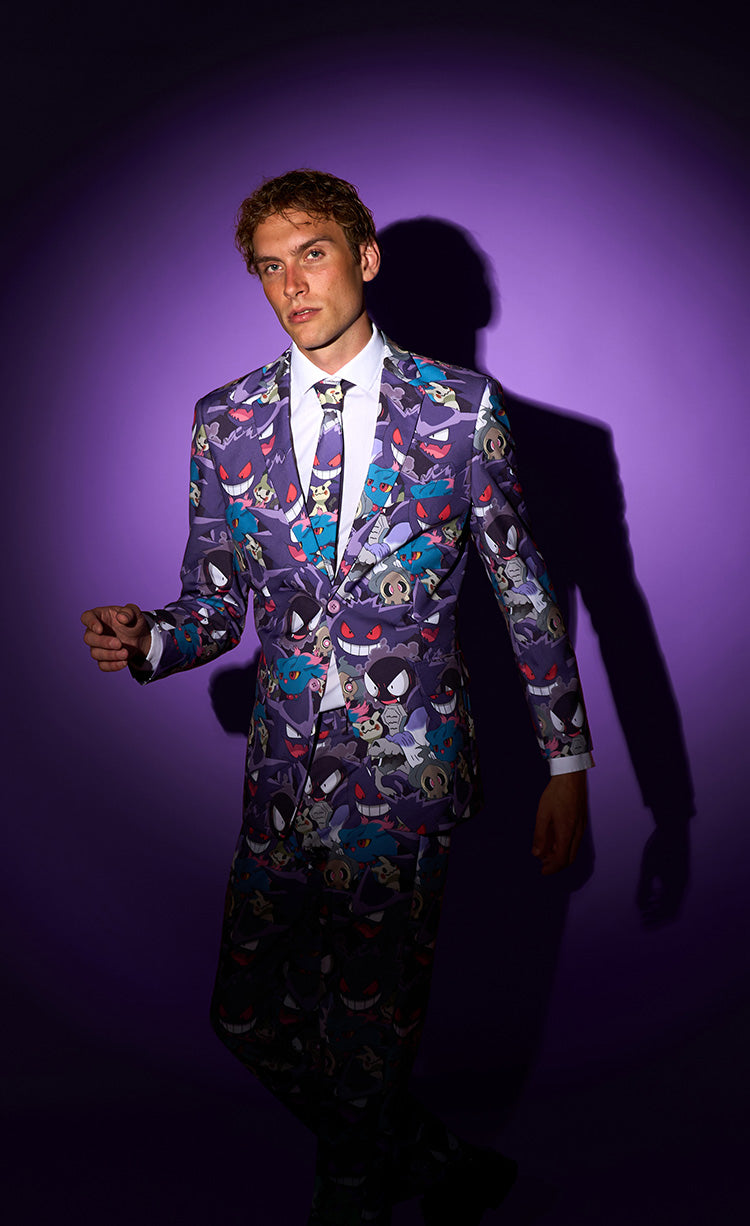 A man wearing a purple suit jacket with a colorful cartoon character print, a white dress shirt, and a patterned tie, standing against a purple spotlight background with a dark shadow.