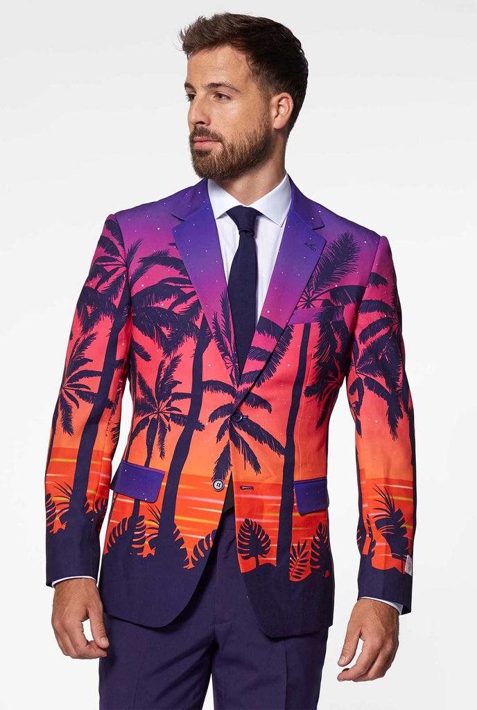 Video of man wearing Suave Sunset men's suit with sunset print, showing suit like a model. Suit consists of blazer, pant and tie.