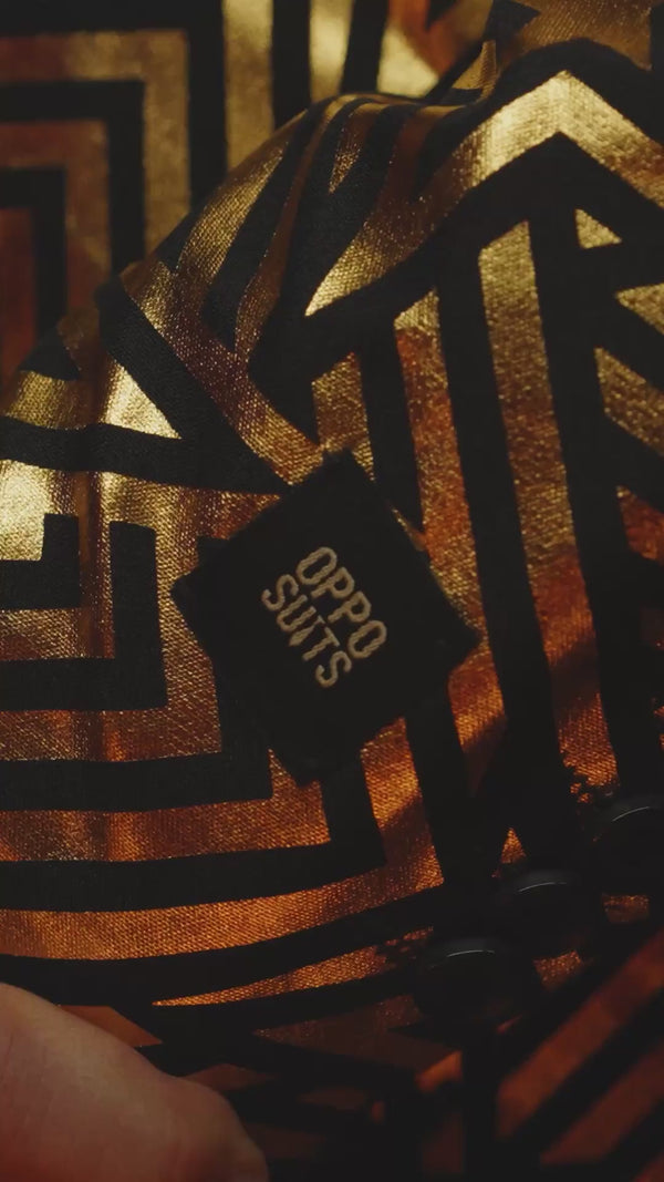 Video of a man wearing the golden geo star suit from Opposuits, showing the suit as a model. With bright lights and flashes. He is also wearing sunglasses in certain shots.