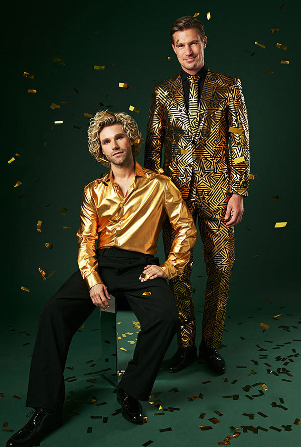 2 men wearing shiny foil print golden outfits, 1 is sitting on a mirror cube.